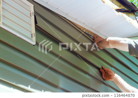 Construction employee installs vinyl plastic siding panels on new house wall facade 116464870