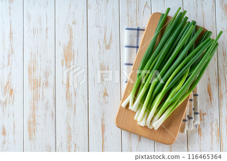 Fresh spring onions or scallions on a cutting board on white wooden table, top view. 116465364