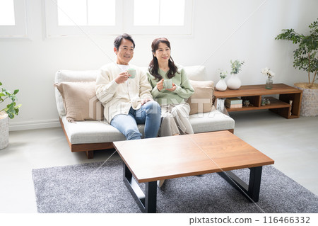 一對 50 多歲的夫婦在客廳放鬆地看電視或影片的全身視圖。 116466332