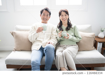 一對50多歲的夫婦的整個身體在客廳裡放鬆地看電視或視頻。 一對50多歲的夫婦的整個身體在客廳裡放鬆地看電視或視頻。 116466334