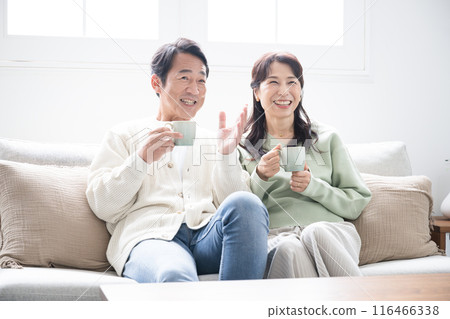 Full-body view of a couple in their 50s relaxing in the living room. Full-body profile of a couple talking Full-body view of a couple in their 50s relaxing in the living room. Full-body profile of a couple talking 116466338