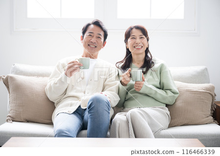 一對 50 多歲的夫婦在客廳放鬆地看電視或影片的全身視圖。 一對 50 多歲的夫婦在客廳放鬆地看電視或影片的全身視圖。 116466339