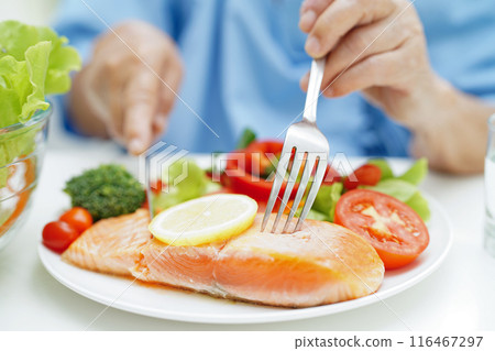 Asian elderly woman patient eating salmon stake and vegetable salad for healthy food in hospital. 116467297