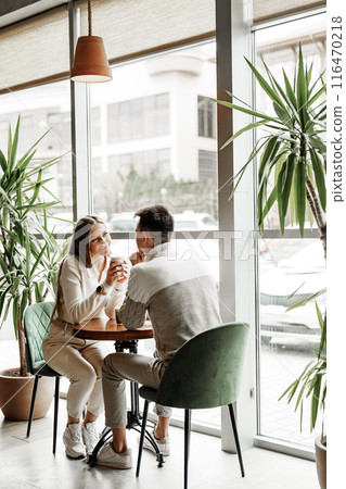 Two Friends Enjoying Casual Conversation Over Coffee at a Modern Cafe During Daytime Two Friends Enjoying Casual Conversation Over Coffee at a Modern Cafe During Daytime 116470218