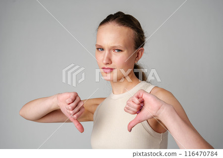 Young Woman Giving Thumbs Down Gesture Against a Neutral Background. Young Woman Giving Thumbs Down Gesture Against a Neutral Background. 116470784
