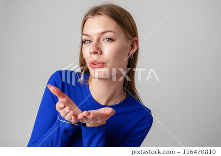 Young Woman in Blue Top Blowing a Kiss Against a Neutral Background. Young Woman in Blue Top Blowing a Kiss Against a Neutral Background. 116470810