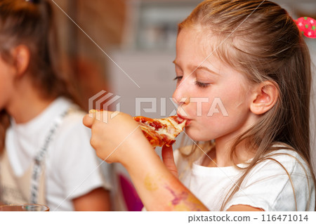 Young Girl Enjoying a Slice of Pizza at a Birthday Party Indoors 116471014