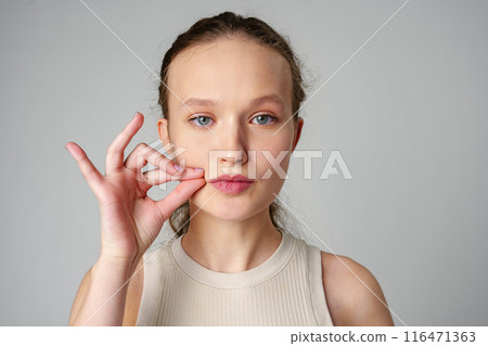 Young Woman Making a Hush Gesture on gray background in studio Young Woman Making a Hush Gesture on gray background in studio 116471363