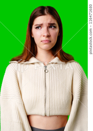Young Woman Expressing Skepticism Standing Against Green Background in Casual Outfit 116471680