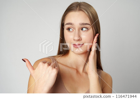 Young Woman in Tank Top Pointing at Something on gray background 116471944