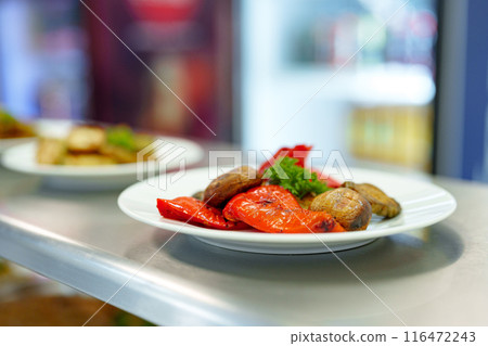 Vibrant Grilled Vegetables Served on a White Plate in a Busy Restaurant Kitchen Vibrant Grilled Vegetables Served on a White Plate in a Busy Restaurant Kitchen 116472243
