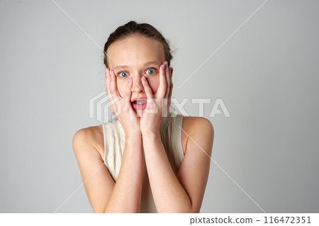 Young Woman Covering Her Face With Her Hands in Fear on gray background 116472351