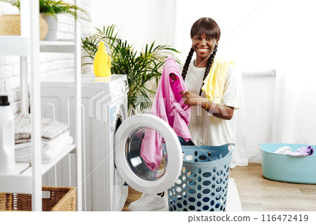 African Woman Folding Laundry After Washing Clothes in Modern Laundry Room 116472419