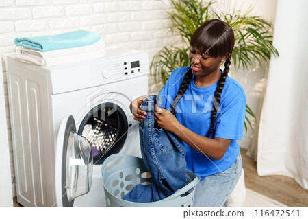 African Woman Loading Laundry Into Washing Machine in Home 116472541