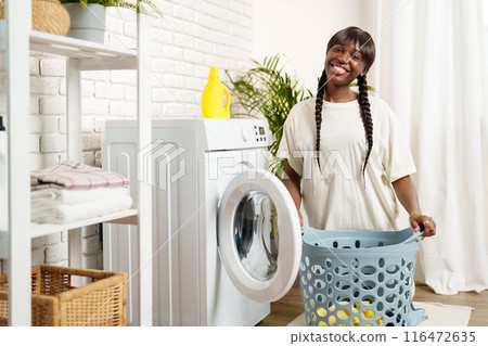 African Woman Loading Laundry Into Washing Machine in Home 116472635