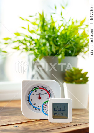 Digital Thermometer Displaying Temperature and Humidity Near Window 116472653