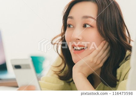 一位 30 多歲的女性在家放鬆，用智慧型手機玩樂 116473598