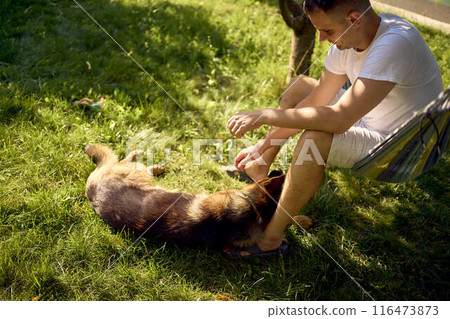 man rests and listens to music in a hammock, his dog rests nearby 116473873
