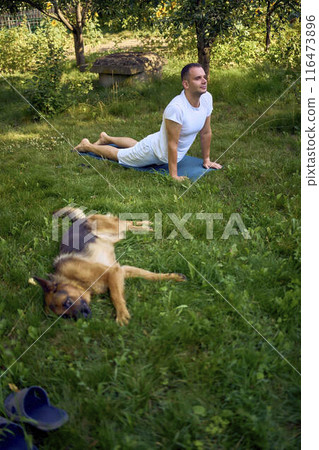 man does somatic exercises with his dog in the garden in the morning 116473896