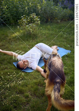 man does somatic exercises with his dog in the garden in the morning 116473901