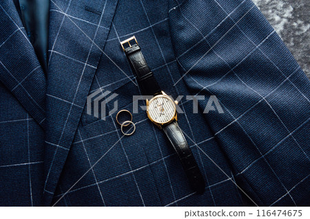Groom's wedding details. Watch, rings and belt placed on a checkered jacket 116474675