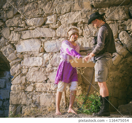 The archaeologist shows a map to a local mercenary of Arab appearance against the backdrop of an ancient fortress. Historical reconstruction of archaeological research of the 19th century 116475054