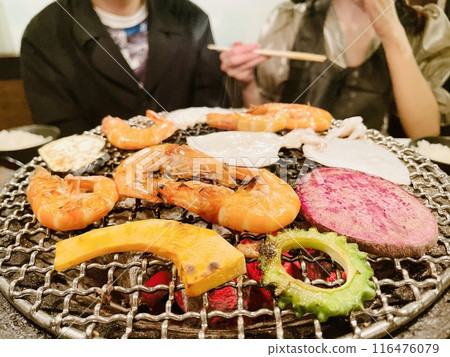 Men and women chatting while grilling seafood and vegetables 116476079
