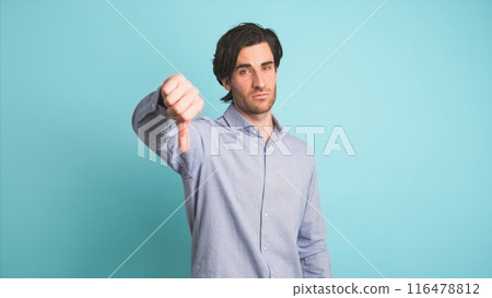 Upset man showing thumb down in blue studio Upset man showing thumb down in blue studio 116478812
