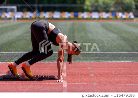Strong female sprinter at the 100m start on starting blocks 116479196