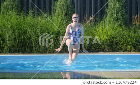 A teenage girl in a striped swimsuit jumping into a backyard pool, enjoying a sunny day. 116479224