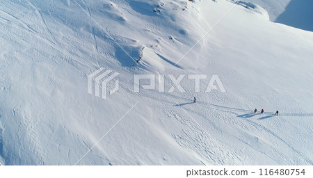 Sportsman people group running winter snow hill trail. Snow-covered slope in Antarctica pristine nature. Men wearing winter gear in cold sunny day. Active sport, tourism, recreation. Aerial top shot 116480754