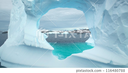 Huge hole in melting iceberg in Antarctic ocean close up. Flight inside frozen glacier cave arch window drifting blue cold water. Arctic winter landscape, global warming problem. Polar climate change 116480788