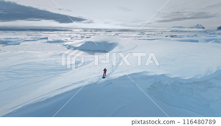 Man standing on glacier in Antarctica make drone panoramic shot of pristine winter Arctic landscape. Snow covered hill, frozen ocean, icebergs, ice floes. Fly over untouched wilderness of Antarctica 116480789