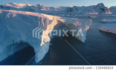 Large impressive iceberg cave in arctic sunset landscape. Huge high ice glacier at polar nature environment. Ecology, melting ice, climate change, global warming. Close up aerial drone shot 116480828