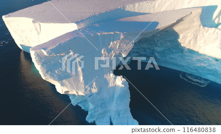 Giant Antarctic blue iceberg cave in sunset bright light. Huge crashed ice glacier at polar nature environment. Ecology, melting ice, climate change and global warming concept. Aerial drone panorama 116480838