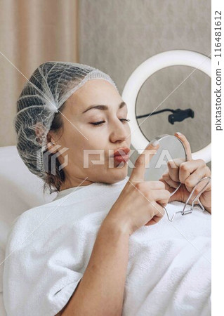 woman carefully observes the effects of her latest skincare treatment, using a mirror to scrutinize her refreshed complexion 116481612