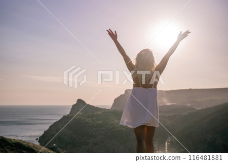 A woman is standing on a hill overlooking a body of water. She is wearing a white dress and she is happy. A woman is standing on a hill overlooking a body of water. She is wearing a white dress and she is happy. 116481881