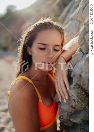 A woman in a yellow and orange bikini is laying on a rock 116481909