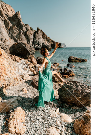 Woman green dress sea. Woman in a long mint dress posing on a beach with rocks on sunny day. Girl on the nature on blue sky background. Woman green dress sea. Woman in a long mint dress posing on a beach with rocks on sunny day. Girl on the nature on blue sky background. 116481940