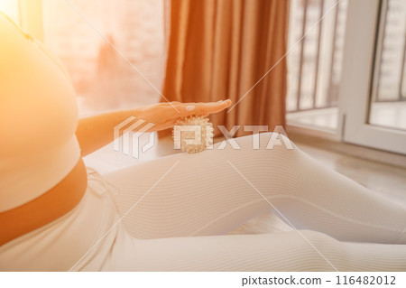 Athletic slim caucasian woman doing thigh self-massage with a massage ball indoors. Self-isolating massage 116482012