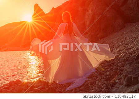 Mysterious woman silhouette long hair walks on the beach ocean water, sea nymph wind listens to the wave. Throws up a long white dress, a divine sunset. Artistic photo from the back without a face Mysterious woman silhouette long hair walks on the beach ocean water, sea nymph wind listens to the wave. Throws up a long white dress, a divine sunset. Artistic photo from the back without a face 116482117