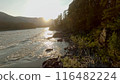 Shooting from a dynamic FPV drone. A flight over a bubbling mountain river with rapids. A flight over the forest and water. Beautiful young woman, standing on a rocky shore. 116482224