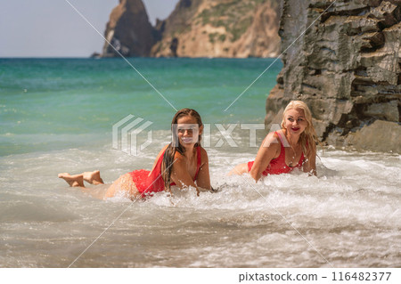Women ocean play. Seaside, beach daytime, enjoying beach fun. Two women in red swimsuits enjoying themselves in the ocean waves. 116482377