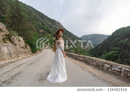 A woman in a white dress is standing on a road with a hat on A woman in a white dress is standing on a road with a hat on 116482428