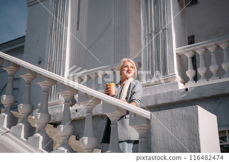 A woman is standing on a white staircase with a cup in her hand. She is smiling and looking up at the sky. A woman is standing on a white staircase with a cup in her hand. She is smiling and looking up at the sky. 116482474