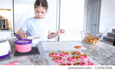 With focused attention, this budding culinary artist dips pretzels into a pot of melted chocolate, creating sweet delights in the warmth of a well-lit home kitchen. With focused attention, this budding culinary artist dips pretzels into a pot of melted chocolate, creating sweet delights in the warmth of a well-lit home kitchen. 116483886