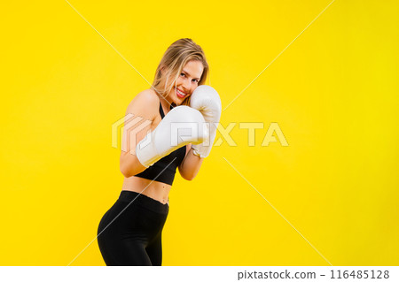 A woman boxer in gloves training on yellow background studio 116485128