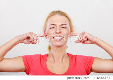 Woman closing ears with fingers, big noise. 116486165