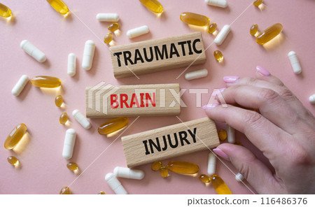 Traumatic Brain Injury symbol. Concept words Traumatic Brain Injury on wooden blocks. Beautiful pink background with pills. Doctor hand. Healthcare and Traumatic Brain Injury concept. Copy space. 116486376