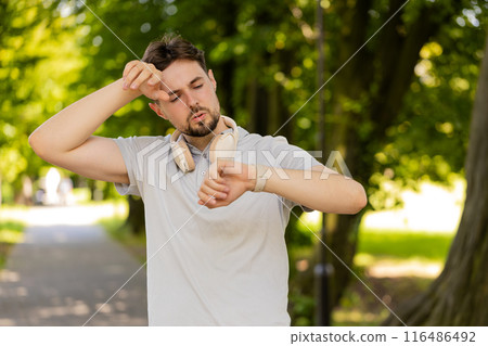 Active young man jogger running in public park and looking at smartwatch, getting tired relaxing Active young man jogger running in public park and looking at smartwatch, getting tired relaxing 116486492